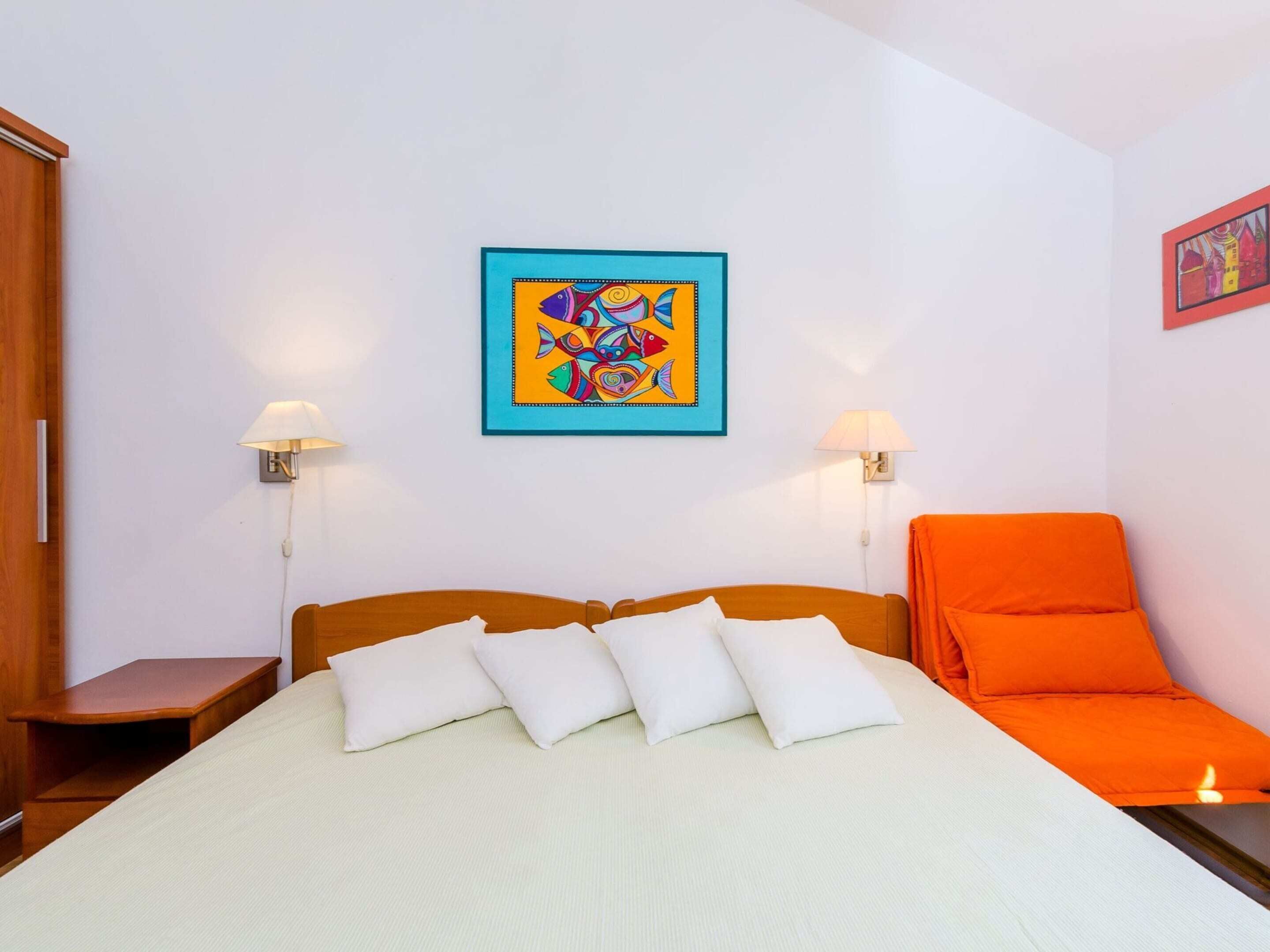 A hotel room with a bed, pillows, a nightstand, a chair, and artwork on the wall.