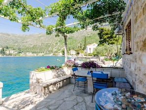 A terrace with stone flooring, a table with chairs, and a view of the sea and hills. - Apartments Lion - One Bedroom Apartment (Dubrovnik)