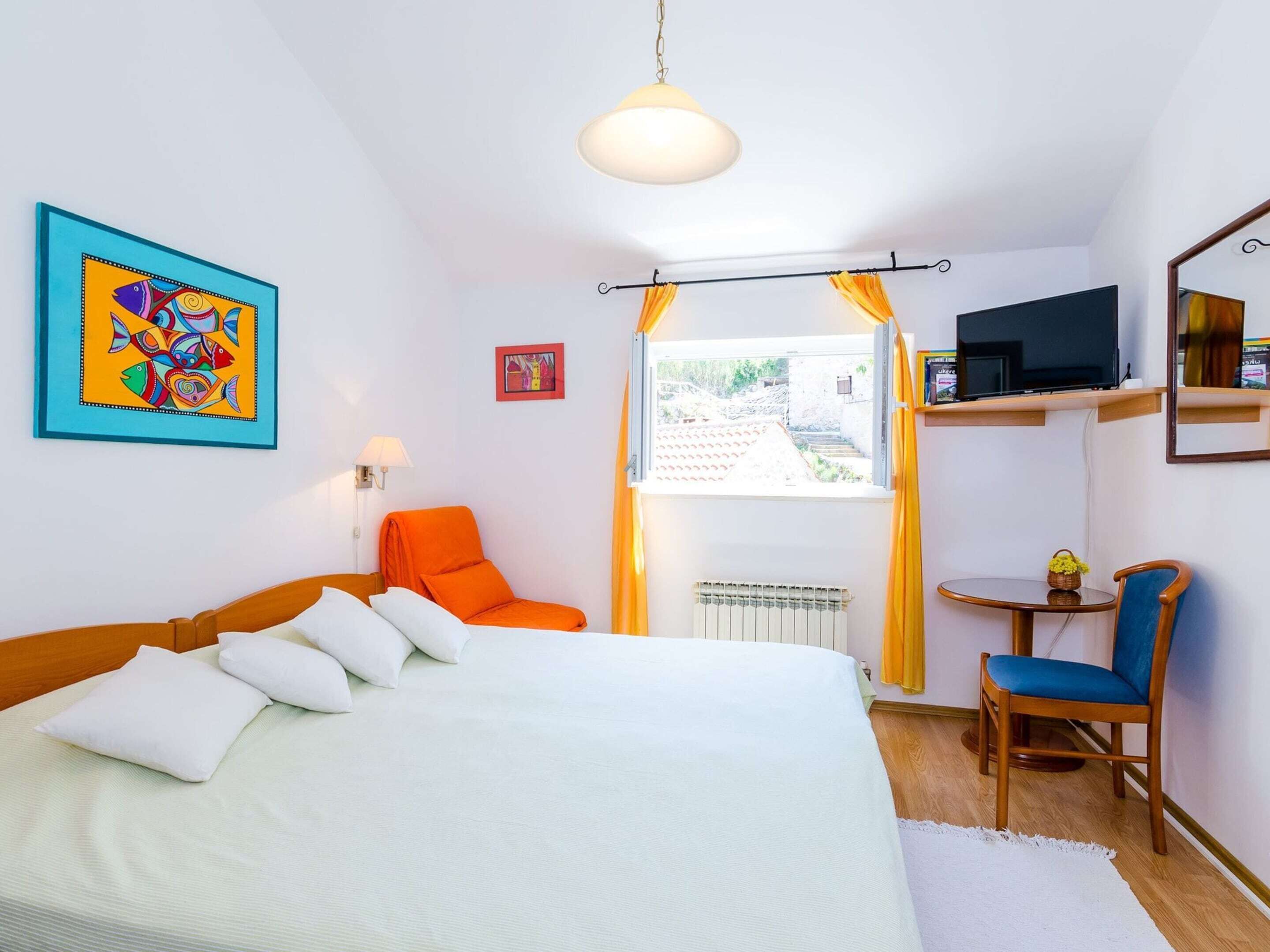 Un dormitorio con una cama, una silla, un televisor y una ventana con cortinas.