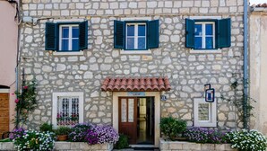 A stone building with three windows, a door, and a small garden area with flowers. - Apartments Lion - One Bedroom Apartment (Dubrovnik)
