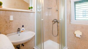 A bathroom with a glass-enclosed shower, a sink with a soap dispenser, a mirror, and a window with blinds. - Apartments Lion - One Bedroom Apartment (Dubrovnik)