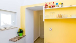 A narrow hallway with a window on the left, a potted plant, and a shelf with various items. - Apartments Lion - One Bedroom Apartment (Dubrovnik)