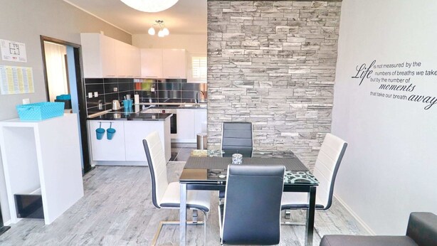 A modern kitchen with black and white cabinets, a dining area with a glass table and black chairs, and a stone accent wall with a motivational quote. - Apartment Marjana Prizba - Two Bedroom Apartment With Terrace and Partial Sea View (Blato)