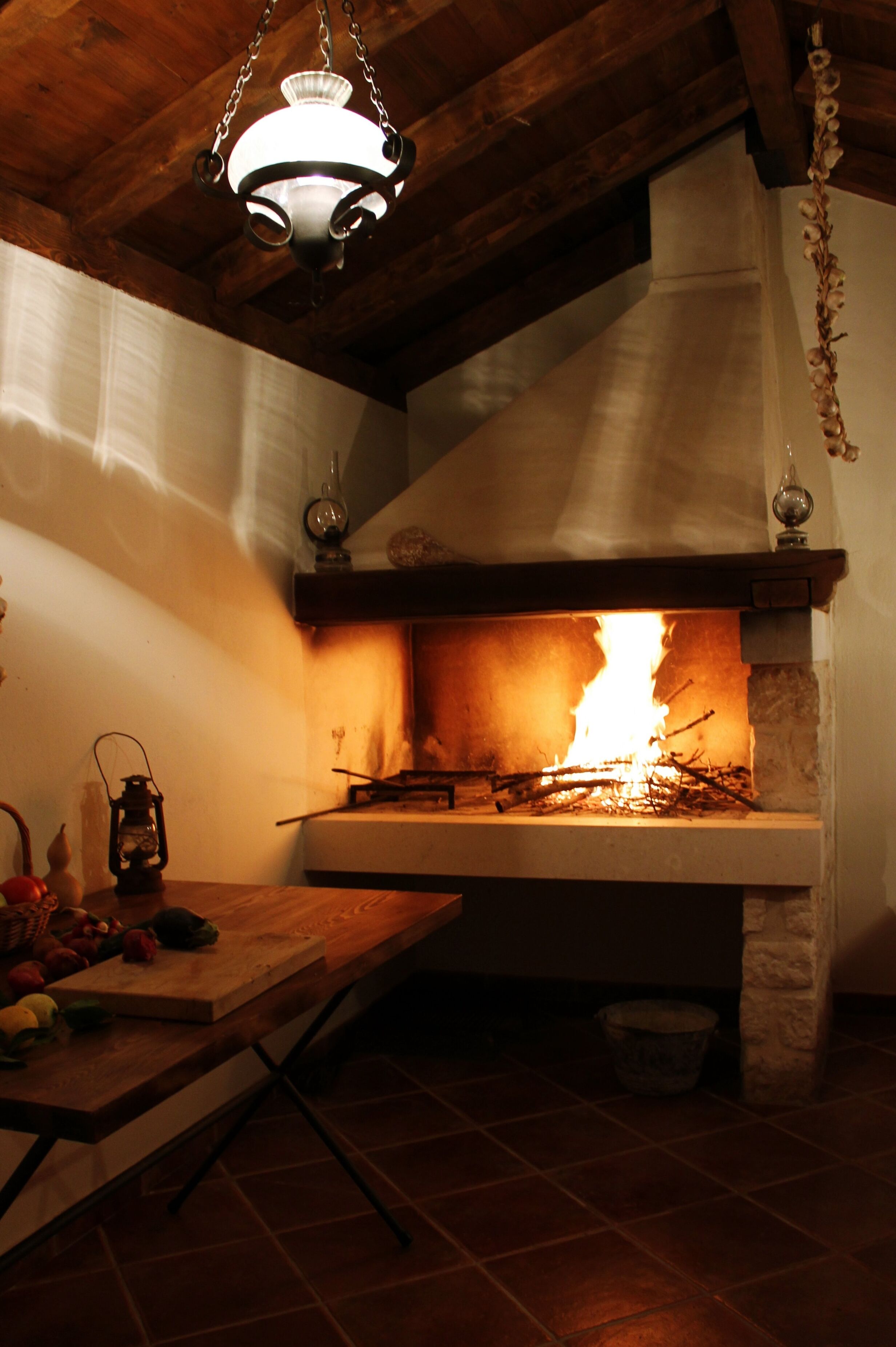 Une cheminée avec un feu apparent, un luminaire suspendu et un plafond en bois rustique.