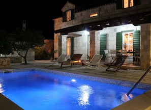 Un espace piscine avec des chaises longues et un bâtiment en pierre doté de volets verts.