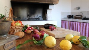 Eine Küche mit einem Holztisch, der mit frischem Obst und Gemüse, einem Schneidebrett und einer Kaffeemühle bestückt ist.