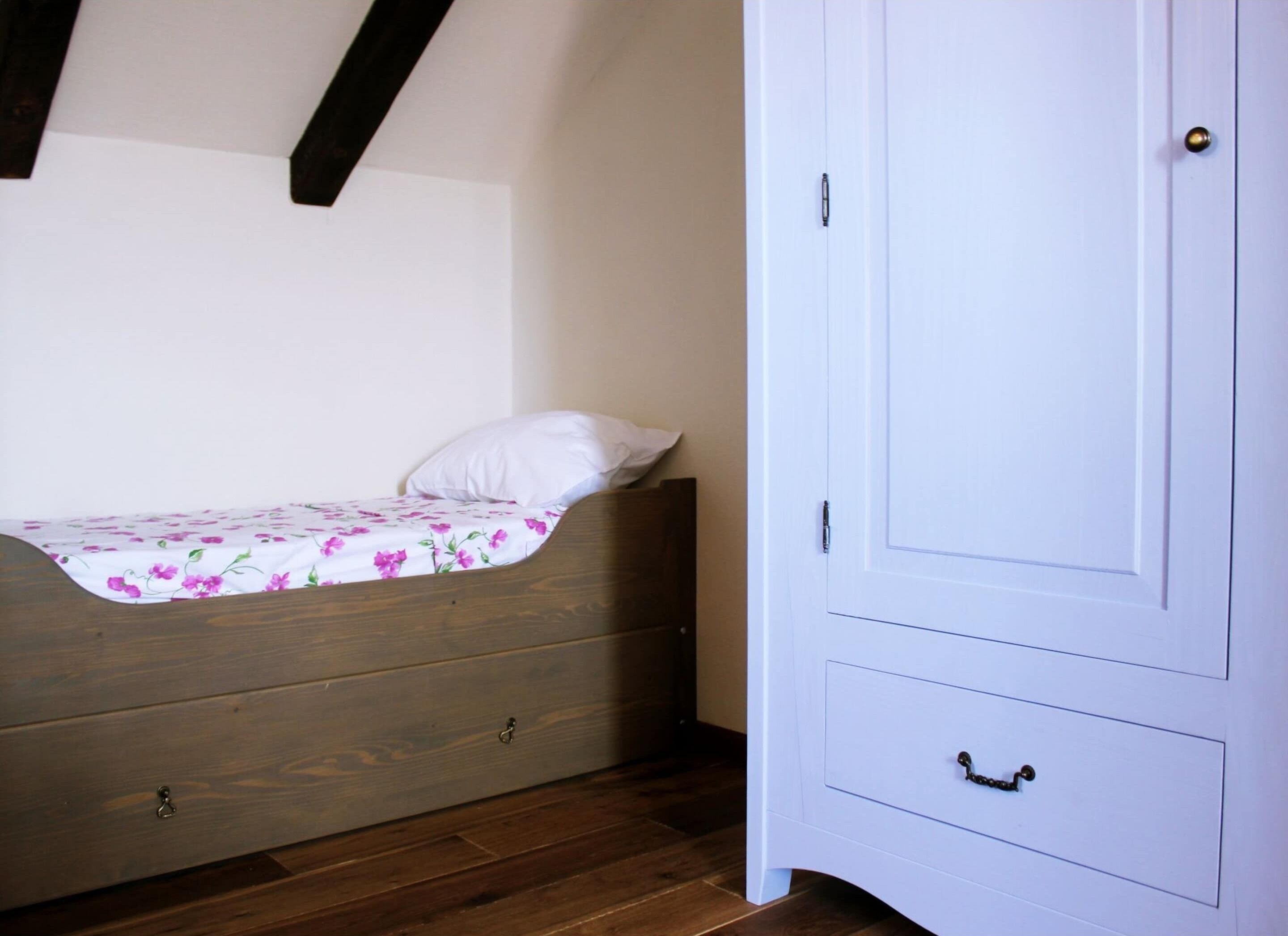 Een slaapkamer met een houten bed, een witte kast en een houten vloer.