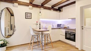 A compact kitchen with white cabinets, a wooden ceiling, a dining table with chairs, a microwave, an oven, and a small potted plant. - Apartment City Gem - Studio (Dubrovnik)