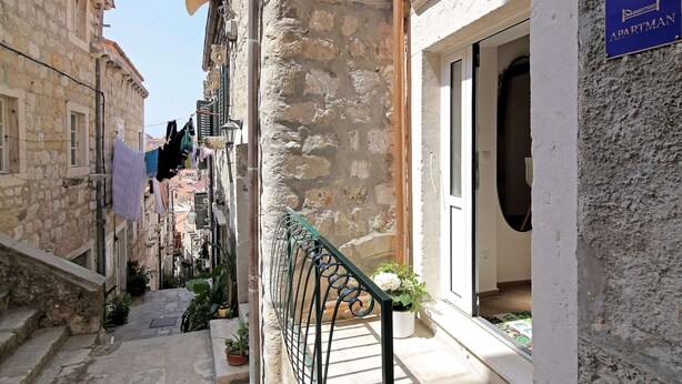 A narrow street with stone buildings, a balcony with a metal railing, and a sign indicating an apartment building. - Apartment City Gem - Studio (Dubrovnik)