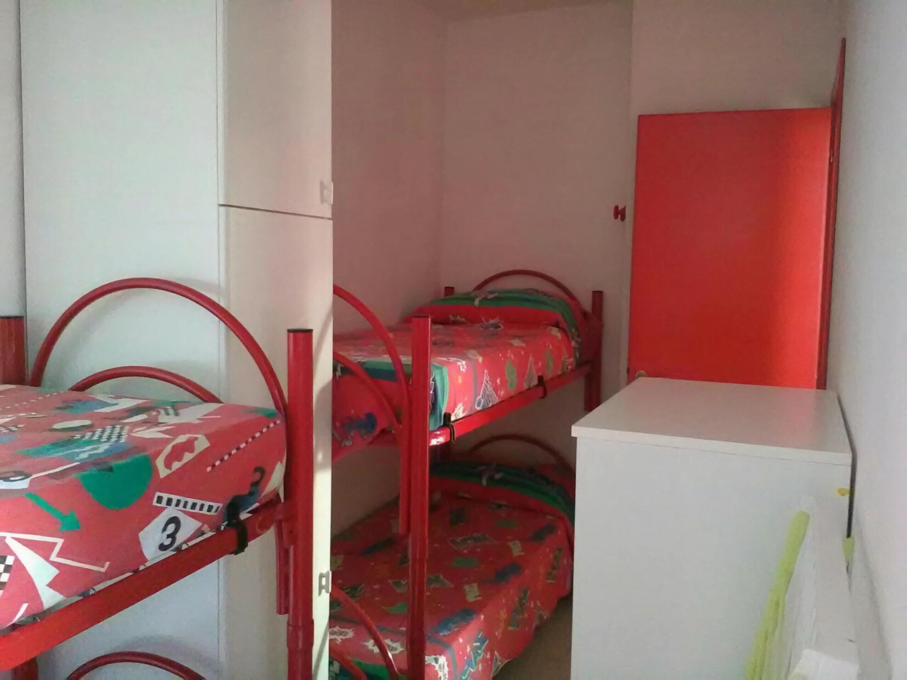 Una habitación con literas, un armario blanco y una puerta roja.