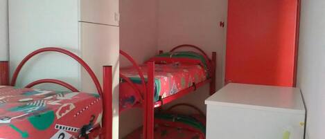 Una habitación con literas, un armario blanco y una puerta roja.