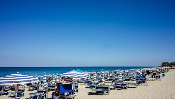 A beach with rows of sun loungers and striped umbrellas. - Holiday Home Near Marina di Mandatoriccio Beach (Mandatoriccio)