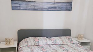 A bedroom with a large bed, floral bedding, two bedside tables with decorative items, and a painting above the bed. - Holiday Home Near Marina di Mandatoriccio Beach (Mandatoriccio)