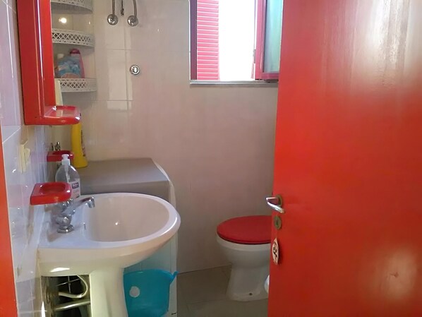 A bathroom with a white sink, red toilet, and a window with blinds.