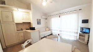 Ein kompakter Wohnraum mit Küchenzeile, Essbereich, Fernseher und einem Balkon mit Vorhängen.