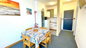 A compact kitchen with a refrigerator, microwave, and a small dining area with a table and chairs. - Holiday Home in Caorle Near Spiaggia Tartaruga (Caorle)