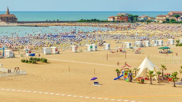 A crowded beach with numerous umbrellas and beach huts. - Holiday Home in Caorle Near Spiaggia Tartaruga (Caorle)