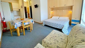 A compact room with a bed, a sofa, a dining table with chairs, and a kitchenette area. - Holiday Home in Caorle Near Spiaggia Tartaruga (Caorle)