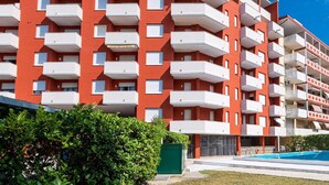 A multi-story residential building with balconies, a swimming pool, and a green bush in the foreground. - Holiday Home in Caorle Near Spiaggia Tartaruga (Caorle)