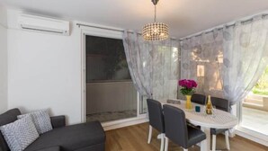 Ein Essbereich mit Tisch, Stühlen und einer Chandelieber. Ein Sofa und ein Fenster mit Vorhängen sind ebenfalls vorhanden.