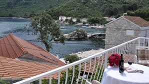 Eine Terrasse mit einem Tisch für zwei Personen, mit Blick auf einen See, im Hintergrund Boote und Häuser.
