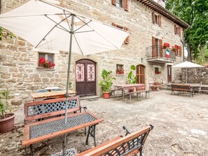A stone building with a courtyard featuring outdoor seating, potted plants, and a large umbrella.