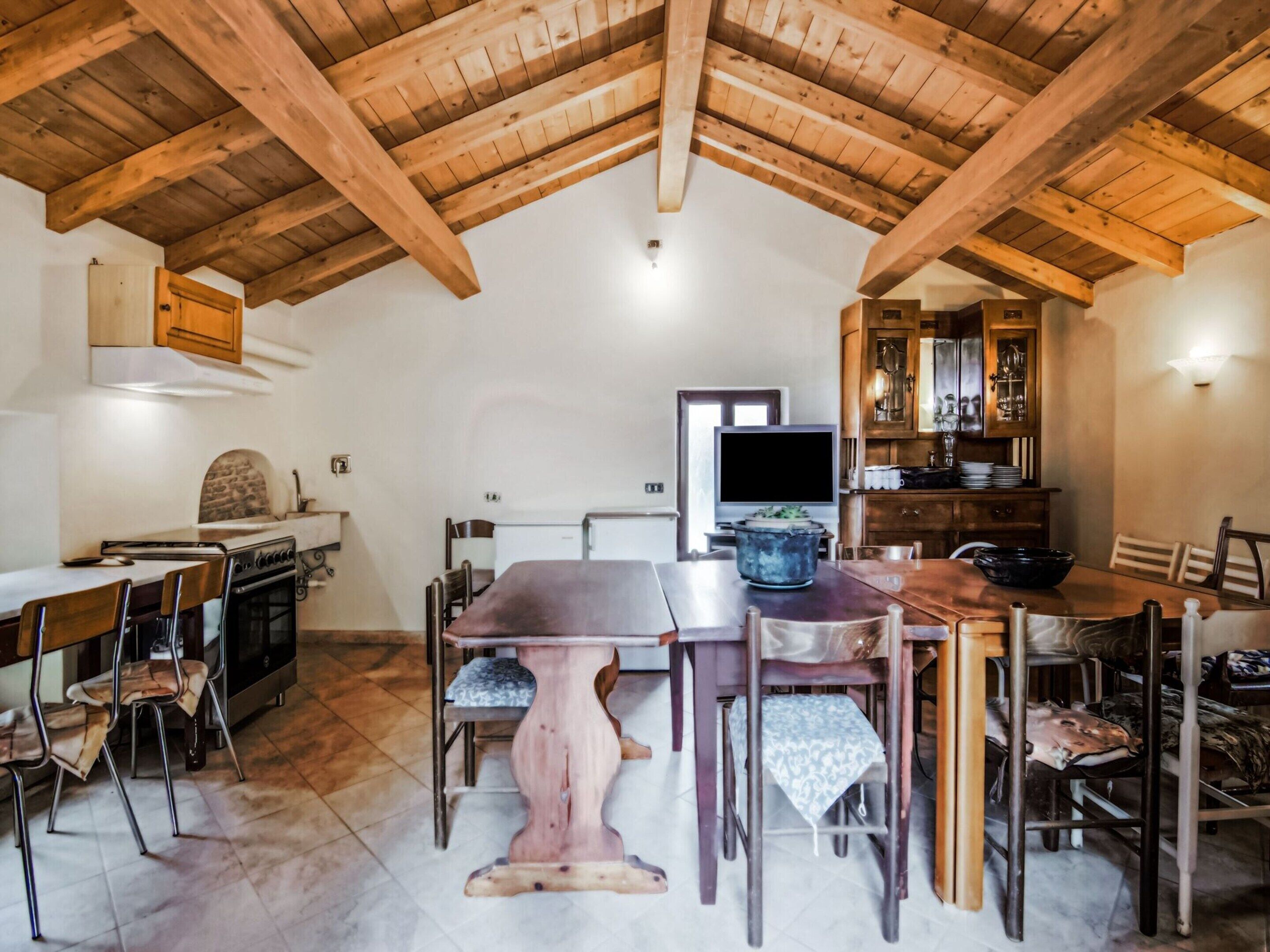 A rustic dining area with a wooden table and chairs, a kitchen with a stove, and a television.