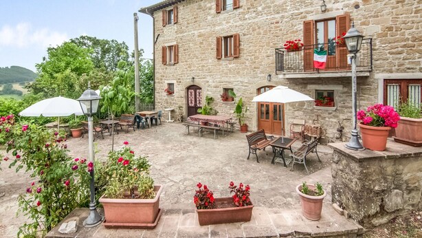 A stone building with outdoor seating, potted plants, and a flag. - Belvilla by OYO Bilocale Monolocale 2adeg Piano (Assisi)