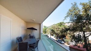 A balcony with a table and chairs, a glass railing, and a view of trees and parked cars. - Apartment Vesna - Superior Three Bedroom Apartment With Balcony (Dubrovnik)