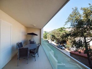 Ein Balkon mit Tisch und Stühlen, einer Glasumlaufung und Blick auf Bäume sowie parkende Autos.