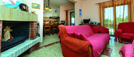 Uma sala de estar com lareira, sofás vermelhos e uma área de jantar com mesa e cadeiras.