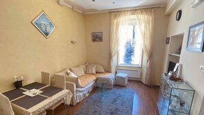 A cozy living room with a sofa, a dining table with chairs, a small round table, and a glass cabinet with dishes.