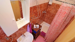 Un baño con lavamanos blanco, espejo y ducha. Hay una toalla rosa y una cortina de ducha con estampado geométrico.