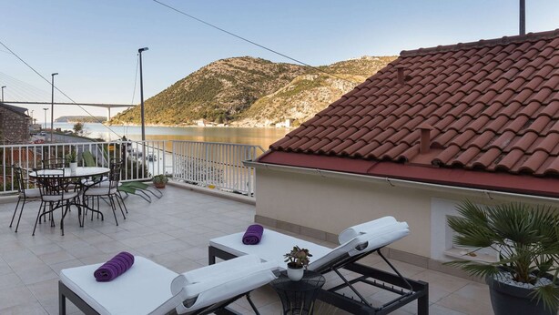 Una terraza con sillones de descanso y una mesa, con vistas a un cuerpo de agua y un puente.