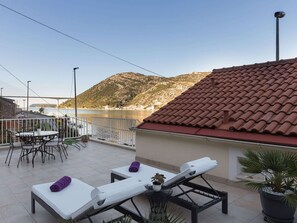A terrace with lounge chairs and a table, overlooking a body of water and a bridge. - Apartment Cetinic - Two Bedroom Apartment With Terrace and Sea View (Dubrovnik)