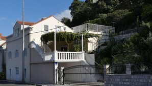 Un edificio de dos pisos con balcón, una escalera y entrada protegida por una reja.