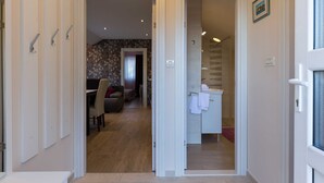 Un pasillo que conduce a un comedor con sofá y mesa, un baño con ducha y lavamanos, y una puerta con pomo.