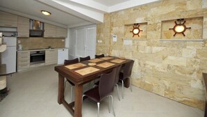 A modern kitchen with built-in appliances, a dining area with a wooden table and chairs, and a stone wall with decorative lighting. - Apartments Villa Moonlight - One Bedroom Apartment With Sea View Balcony (Okrug)