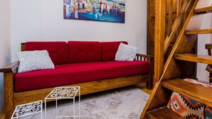 A red sofa with white cushions, a wooden table with a geometric pattern, and a staircase with a patterned cushion. - Holiday Home St George - Two Bedroom Apartment With City View (Dubrovnik)