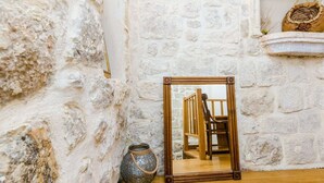 A rustic room with a stone wall, a wooden chair, and a mirror reflecting the room. - Holiday Home St George - Two Bedroom Apartment With City View (Dubrovnik)