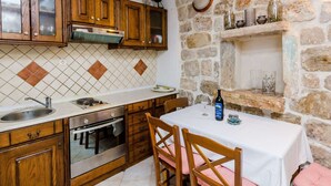 A kitchen with wooden cabinets, a stone wall, a built-in oven, and a dining table with chairs. - Holiday Home St George - Two Bedroom Apartment With City View (Dubrovnik)