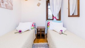 A cozy bedroom with two single beds, a small table, a mirror, and a window with curtains. - Holiday Home St George - Two Bedroom Apartment With City View (Dubrovnik)