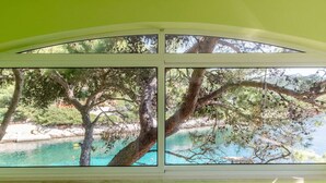 A room with a large window overlooking a turquoise sea and a tree-lined beach. - Seafront Apartments Olivera-one Bedroom Apartment With Balcony and Sea View (Blato)