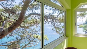 A room with a large window overlooking a body of water, a stone structure, and a red chair. - Seafront Apartments Olivera-one Bedroom Apartment With Balcony and Sea View (Blato)