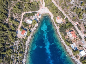 Une vue aérienne d’une zone côtière aux eaux bleues et limpides, bordée d’une végétation luxuriante et ponctuée de plusieurs bâtiments aux toits rouges.
