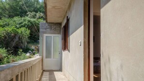 A narrow corridor with a concrete railing, a door with frosted glass panels, and a small room with a bed visible through an open door. - Seafront Apartments Olivera-one Bedroom Apartment With Balcony and Sea View (Blato)
