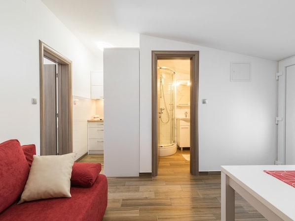 A modern apartment with a red sofa, a white table, and a shower room visible through an open door.