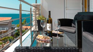 Ein Balkon mit Glastisch, Korbmöbeln, einer Weinflasche und einem Glas.