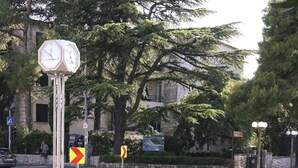 A clock tower with two clocks, surrounded by trees and a flower bed. - Apartment Goge - One-bedroom Apartment With Balcony (Dubrovnik)