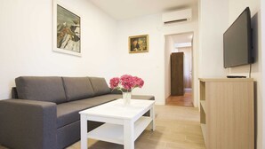 A modern living room with a grey sofa, a white coffee table with a vase of flowers, a flat-screen TV, and a wooden cabinet. - Apartment Goge - One-bedroom Apartment With Balcony (Dubrovnik)